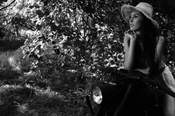 Jovem mulher sexy com cabelos longos ondulados em roupas de couro e óculos de sol posando perto de uma motocicleta. Foto em preto e branco . — Fotografia de Stock