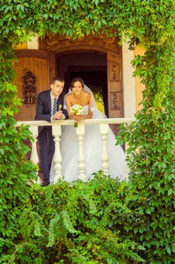 Gelin ve damat yeşil yapraklarla birlikte balkonda poz veriyorlar.