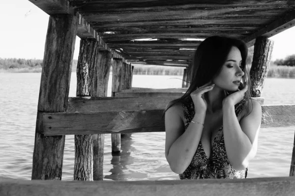 Atractiva mujer rubia sentada en el muelle junto al lago con fondo natural. Novia romántica con vestido blanco y ramo de flores —  Fotos de Stock