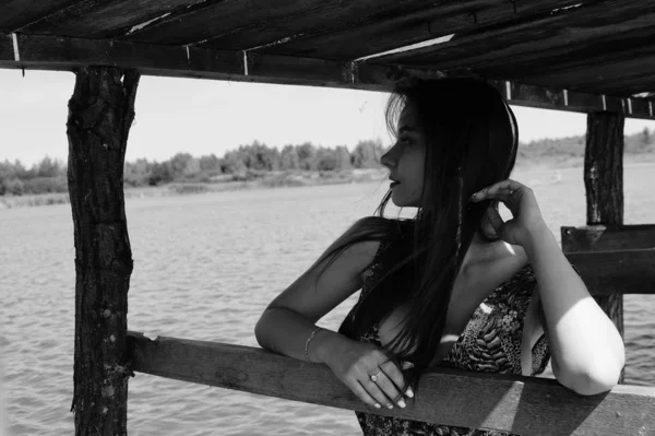 迷人的金发女郎坐在码头旁边的湖与自然背景。浪漫新娘身穿白色连衣裙, 捧花花束 — 图库照片