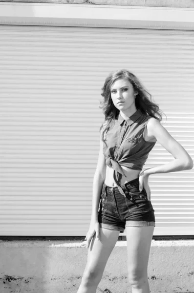 Brünettes asiatisches Mädchen auf dem Dach vor blauem Himmel und modernen Häusern. Junge Frau mit fliegenden Haaren trägt lässiges Kleid - Jeans Shorts schwarzes Hemd — Stockfoto