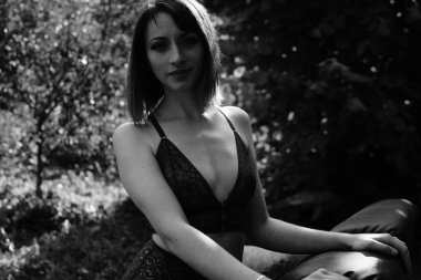 Koyu renk iç çamaşırı giymiş genç ve güzel bir kadın. Elinde tahta evin yanındaki deri koltukta poz veriyor. 