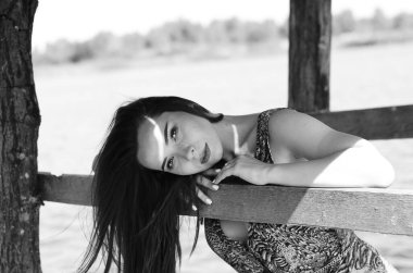 İskele doğa arka plan ile göl yanındaki oturan çekici sarışın bir kadın. Beyaz elbise giyen ve çiçek buketi holding romantik gelin.