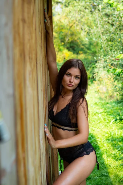 穿着深色内衣裤的年轻貌美的黑发女子站在室外木屋附近 — 图库照片
