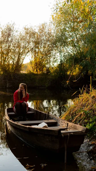 Fille bouclée assis sur le bord d'un bateau en bois abandonné au coucher du soleil . — Photo