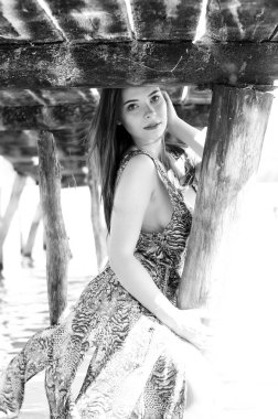 Gölün oradaki tahta iskelede poz veren siyah saçlı kadın. Sırtı Neusiedl Gölü 'nün tahta yaya köprüsüne dönmüş bir kadın. Arka plandaki kayıkhanede güneş yansımaları.