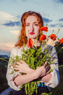 Güzel, bronzlaşmış, beyaz işlemeli elbiseli bir kız elinde bir buket çivi tutuyordu. Mutlu, gülümseyen kadın eğleniyor, sahada yürüyor. Kırsal yaşam tarzı kavramı, ulusal gelenekler.