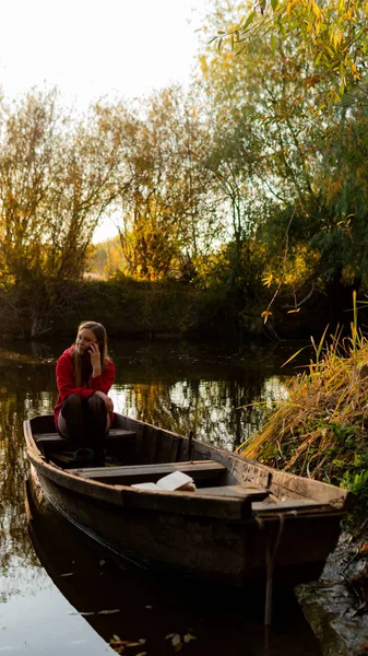 Curly girl sitting on the edge of an abandoned wooden boat at sunset. — Stock Photo, Image