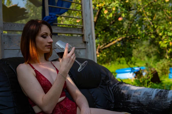 Jeune femme se détendre et boire un verre de vin rouge sur le balcon au coucher du soleil le soir . — Photo