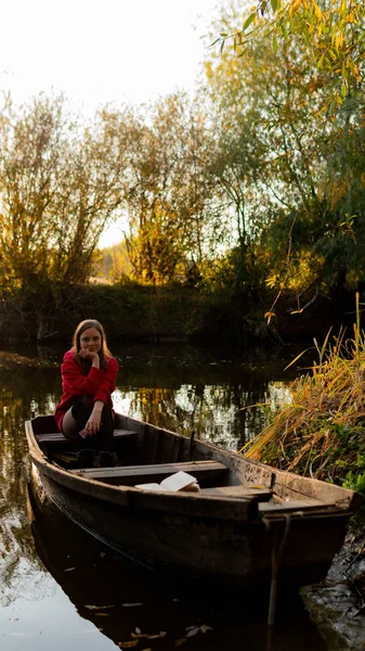 Curly girl sitting on the edge of an abandoned wooden boat at sunset. — Stock Photo, Image