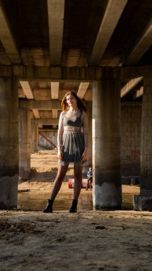 Siyah elbiseli genç kız köprünün altında poz veriyor.