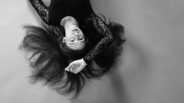 Siyah elbiseli genç bir kadın koyu bir arka planda poz veriyor, siyah saçlı ve kaslı bir spor figürü..