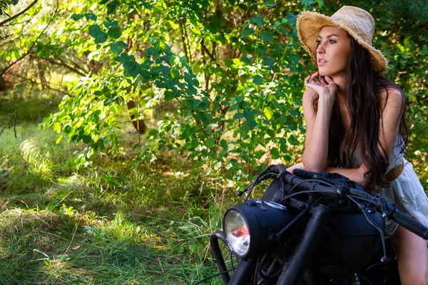 Jonge sexy vrouw met lang golvend haar in lederen kleding en zonnebril poseren in de buurt van een motorfiets. Zwart-wit foto. — Stockfoto