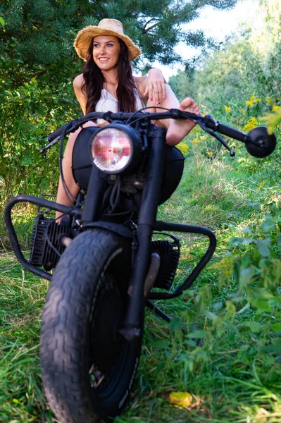 Jeune femme sexy avec de longs cheveux ondulés dans des vêtements en cuir et des lunettes de soleil posant près d'une moto. Photo noir et blanc. — Photo