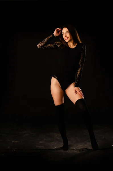 Mujer joven en un body negro posando sobre un fondo oscuro, pelo negro y una figura deportiva muscular . —  Fotos de Stock