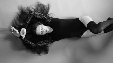 Siyah elbiseli genç bir kadın koyu bir arka planda poz veriyor, siyah saçlı ve kaslı bir spor figürü..