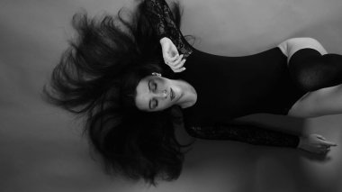 Siyah elbiseli genç bir kadın koyu bir arka planda poz veriyor, siyah saçlı ve kaslı bir spor figürü..