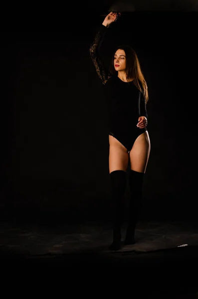 Jovem mulher em um bodysuit preto posando em um fundo escuro, cabelo preto e uma figura esportiva muscular . — Fotografia de Stock