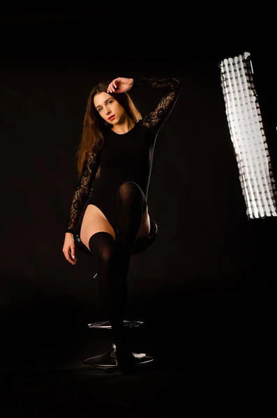 Young woman in a black bodysuit posing on a dark background, black hair and a muscular sports figure. — Stock Photo, Image