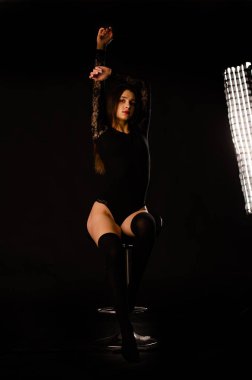 Siyah elbiseli genç bir kadın koyu bir arka planda poz veriyor, siyah saçlı ve kaslı bir spor figürü..