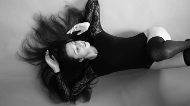 Siyah elbiseli genç bir kadın koyu bir arka planda poz veriyor, siyah saçlı ve kaslı bir spor figürü..