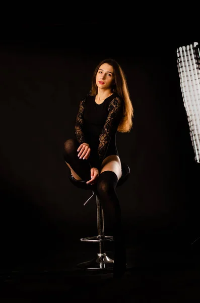 Mujer joven en un body negro posando sobre un fondo oscuro, pelo negro y una figura deportiva muscular . — Foto de Stock