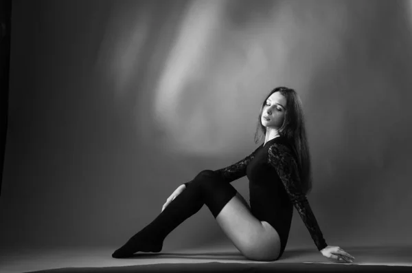 Mujer joven en un body negro posando sobre un fondo oscuro, pelo negro y una figura deportiva muscular . — Foto de Stock