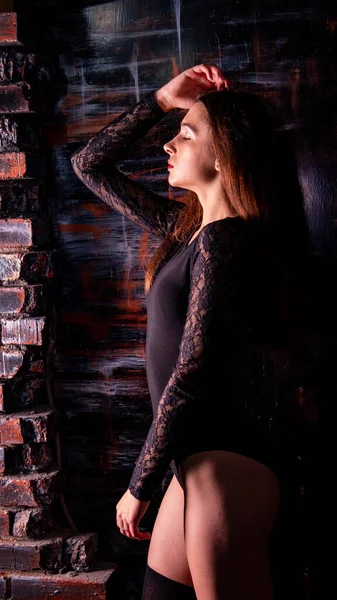 Молода жінка в чорному комбінезоні позує на темному тлі, чорне волосся і м'язистої спортивної фігури — стокове фото