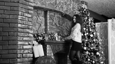 Noel ağacının arka planında hediye kutusu olan, siyah etekli, koyu kahverengi saçlı, seksi, güzel bir kız. Yılbaşı fotoğraf çekimi