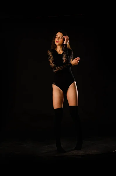 Jeune femme en body noir posant sur fond sombre, cheveux noirs et une silhouette sportive musclée. — Photo