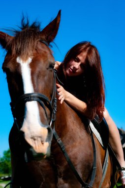 Kırsalda kameraya poz veren çekici genç bir kadın, atın üstünde oturuyor.