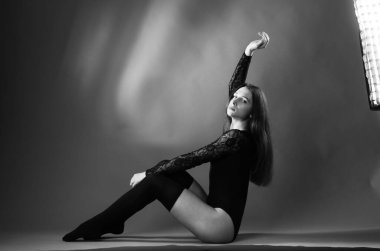 Siyah elbiseli genç bir kadın koyu bir arka planda poz veriyor, siyah saçlı ve kaslı bir spor figürü..