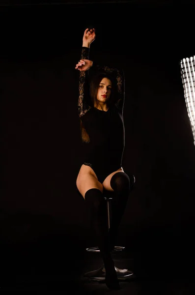 Mujer joven en un body negro posando sobre un fondo oscuro, pelo negro y una figura deportiva muscular . — Foto de Stock