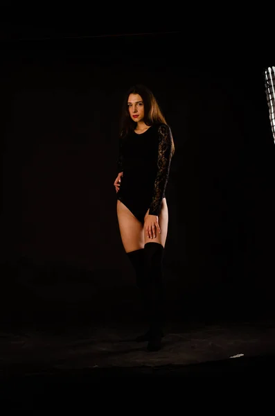 Jovem mulher em um bodysuit preto posando em um fundo escuro, cabelo preto e uma figura esportiva muscular . — Fotografia de Stock