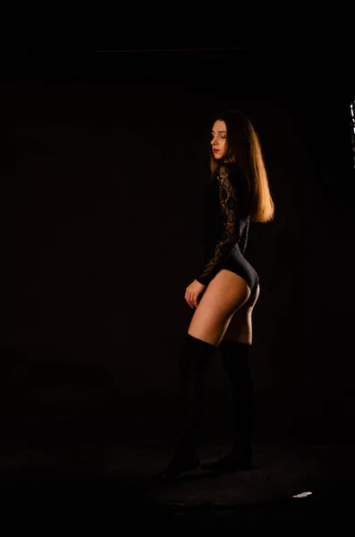 Jovem mulher em um bodysuit preto posando em um fundo escuro, cabelo preto e uma figura esportiva muscular . — Fotografia de Stock