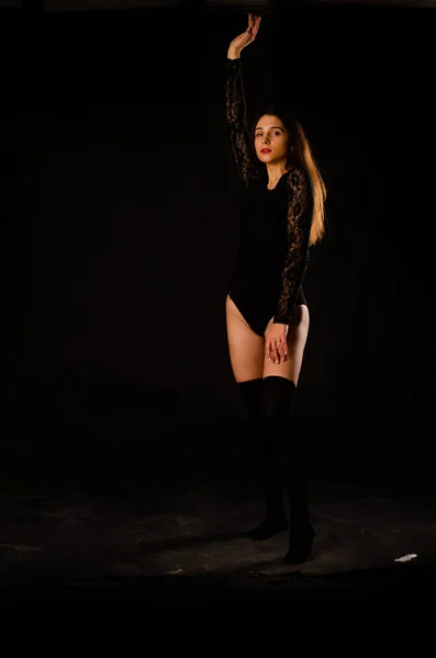 Mujer joven en un body negro posando sobre un fondo oscuro, pelo negro y una figura deportiva muscular . — Foto de Stock