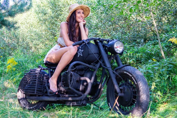 Jeune femme sexy avec de longs cheveux ondulés dans des vêtements en cuir et des lunettes de soleil posant près d'une moto. Photo noir et blanc. — Photo