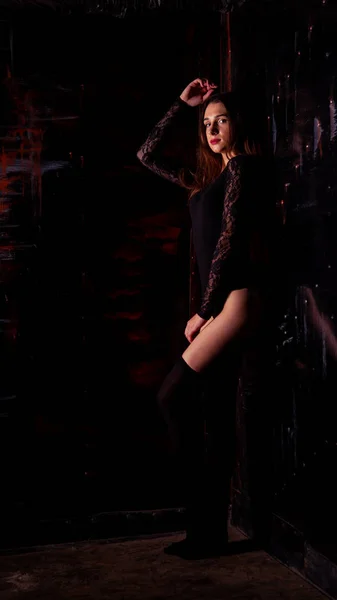 Jovem mulher em um bodysuit preto posando em um fundo escuro, cabelo preto e uma figura esportiva muscular — Fotografia de Stock
