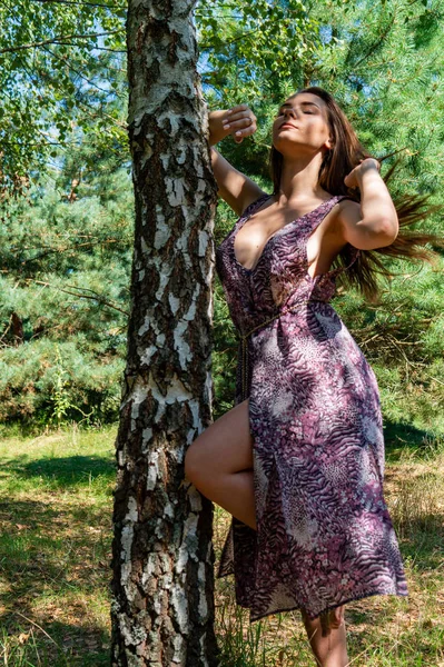 Tmavovlasá žena pózující u dřevěného mola u jezera. Žena v letních šatech se otočila zády k dřevěnému lávkovému můstku Neziderského jezera. Sluneční odrazy v loděnici v pozadí. — Stock fotografie