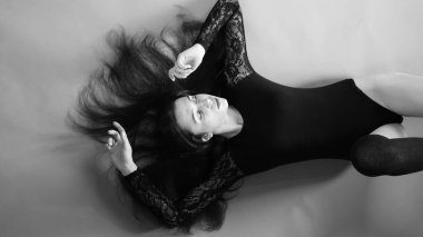 Siyah elbiseli genç bir kadın koyu bir arka planda poz veriyor, siyah saçlı ve kaslı bir spor figürü..