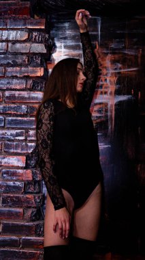 Siyah elbiseli genç bir kadın koyu bir arka planda poz veriyor, siyah saçlı ve kaslı bir spor figürü.