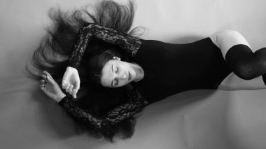 Siyah elbiseli genç bir kadın koyu bir arka planda poz veriyor, siyah saçlı ve kaslı bir spor figürü..