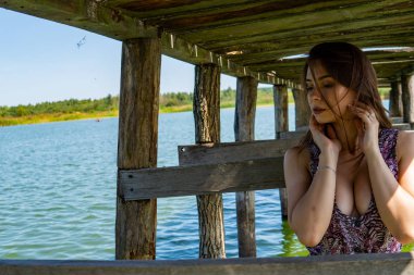 Gölün oradaki tahta iskelede poz veren siyah saçlı kadın. Sırtı Neusiedl Gölü 'nün tahta yaya köprüsüne dönmüş bir kadın. Arka plandaki kayıkhanede güneş yansımaları.