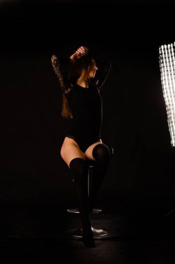 Siyah elbiseli genç bir kadın koyu bir arka planda poz veriyor, siyah saçlı ve kaslı bir spor figürü..