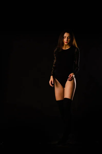 Jonge vrouw in een zwart bodysuit poseren op een donkere achtergrond, zwart haar en een gespierde sportfiguur. — Stockfoto