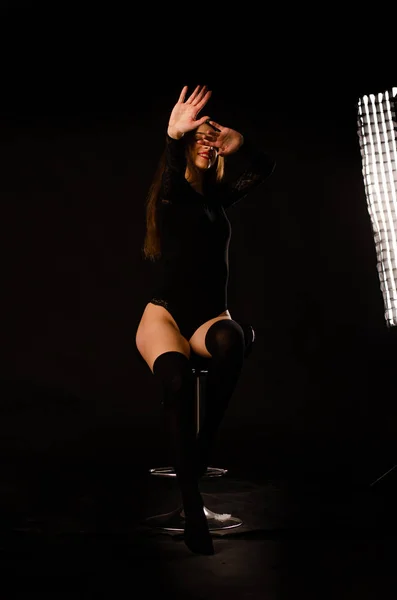 Mujer joven en un body negro posando sobre un fondo oscuro, pelo negro y una figura deportiva muscular . — Foto de Stock