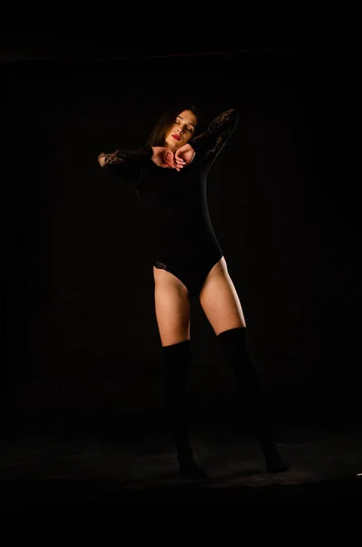 Ung kvinna i svart body suit poserar på en mörk bakgrund, svart hår och en muskulös sport figur. — Stockfoto
