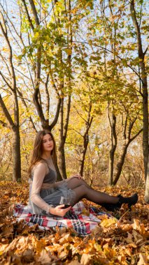 Genç ve güzel bir kadın Sonbaharda parkta bir bardak şarapla