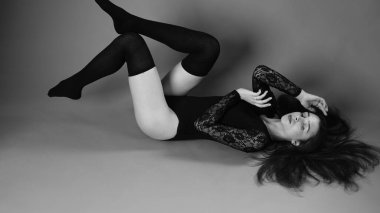 Siyah elbiseli genç bir kadın koyu bir arka planda poz veriyor, siyah saçlı ve kaslı bir spor figürü..