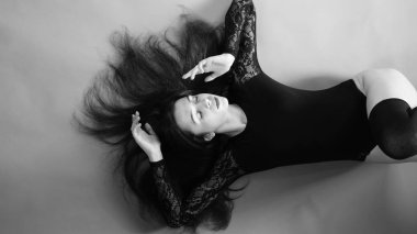 Siyah elbiseli genç bir kadın koyu bir arka planda poz veriyor, siyah saçlı ve kaslı bir spor figürü..